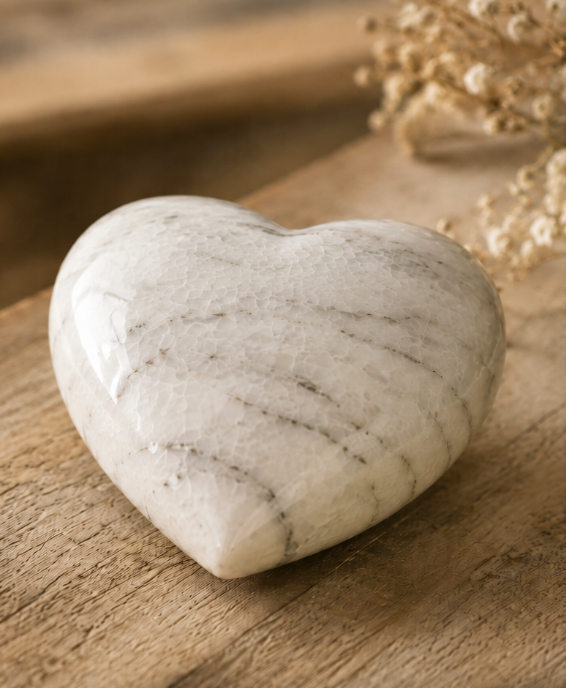 A white marble heart urn resting on weathered wood beside dried gypsophila