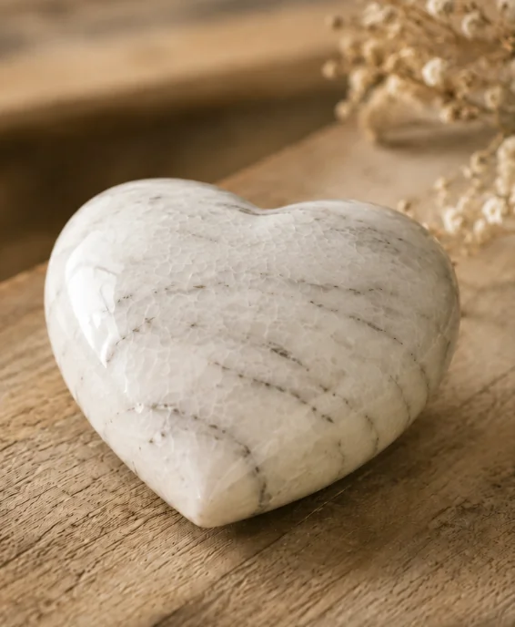 A white marble heart urn resting on weathered wood beside dried gypsophila